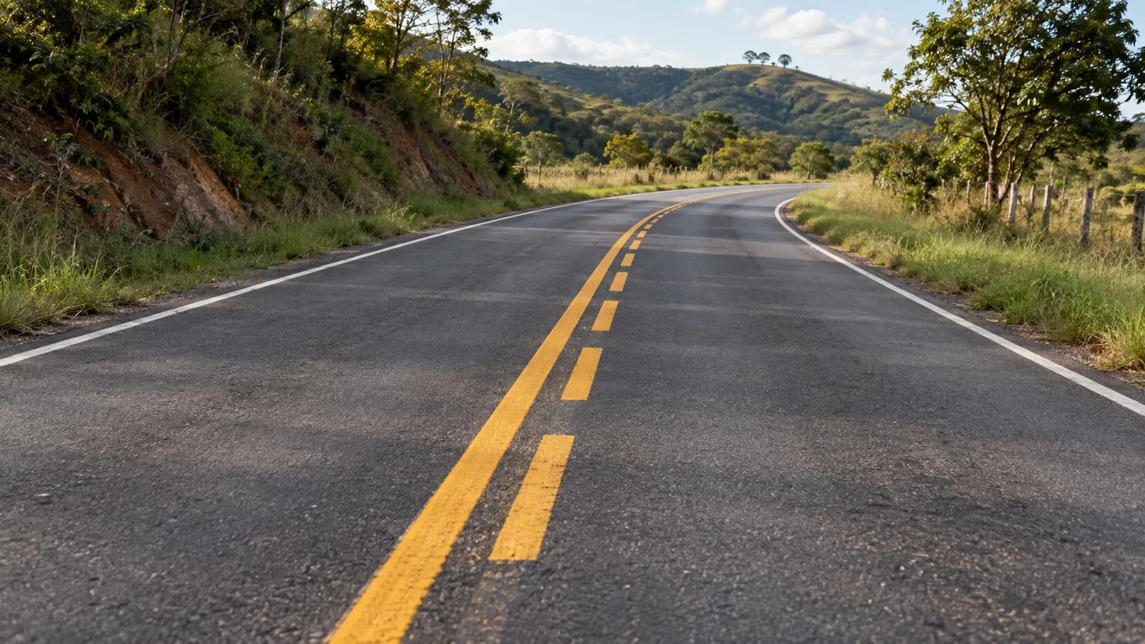 Linha amarela contínua ao lado de uma linha seccionada separa os sentidos de uma estrada tranquila.