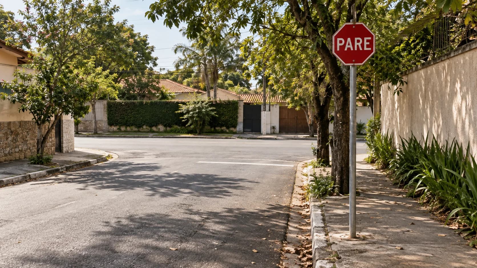 Placa PARE à direita de uma rua arborizada, antes de uma esquina.