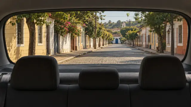 Pelo vidro traseiro e acima dos encostos do banco, vê-se um longo trecho de rua residencial com casas e calçadas, sem veículos próximos.