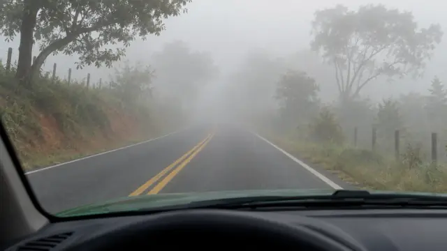 Estrada durante o dia desaparece gradualmente na neblina, vista do interior do carro.